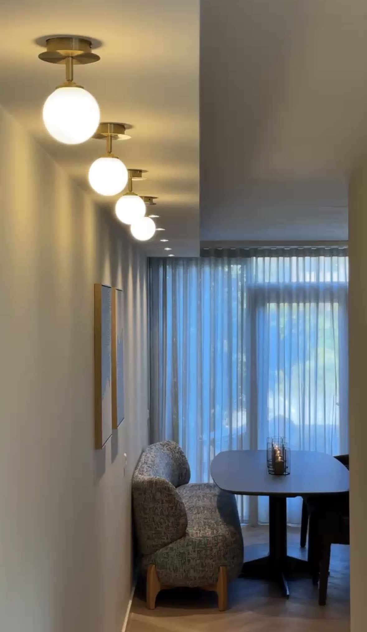 Een rij bollampen met messing armaturen in het plafond van de gang, met zicht op de eethoek
