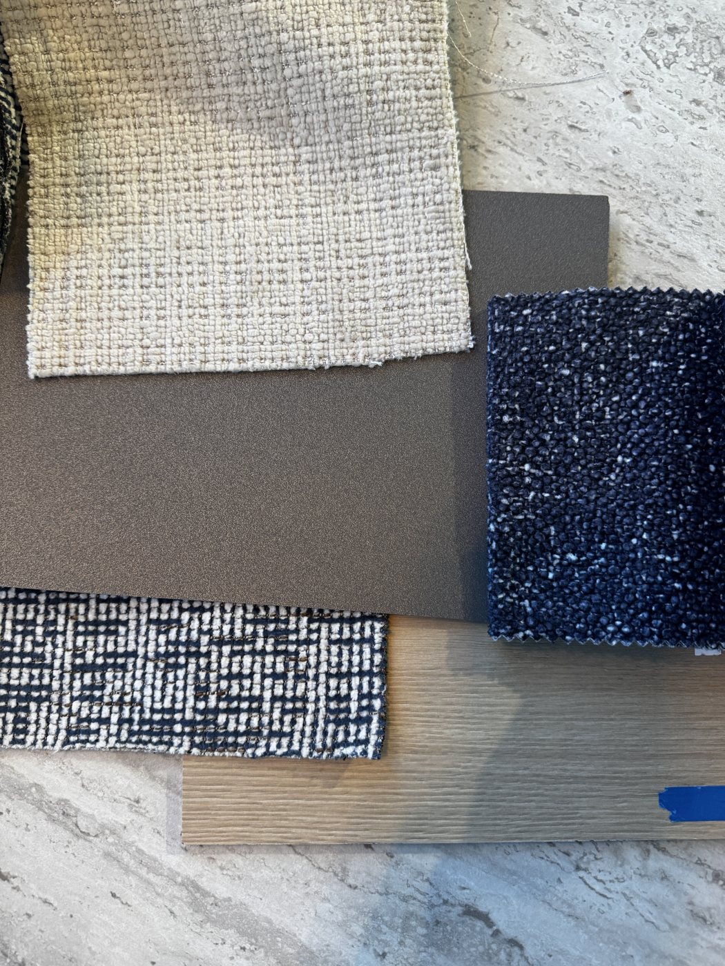 De stalen voor Capelle: een lichte en een donkerblauwe bouclé, een blauw-wit geweven stof, een donkere laminaatplaat en een lichte houten vloer