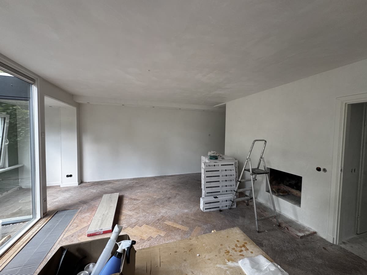 De woonkamer na het stucwerk, met strakke witte wanden en plafond en de pakken nieuwe vloer klaar om te leggen